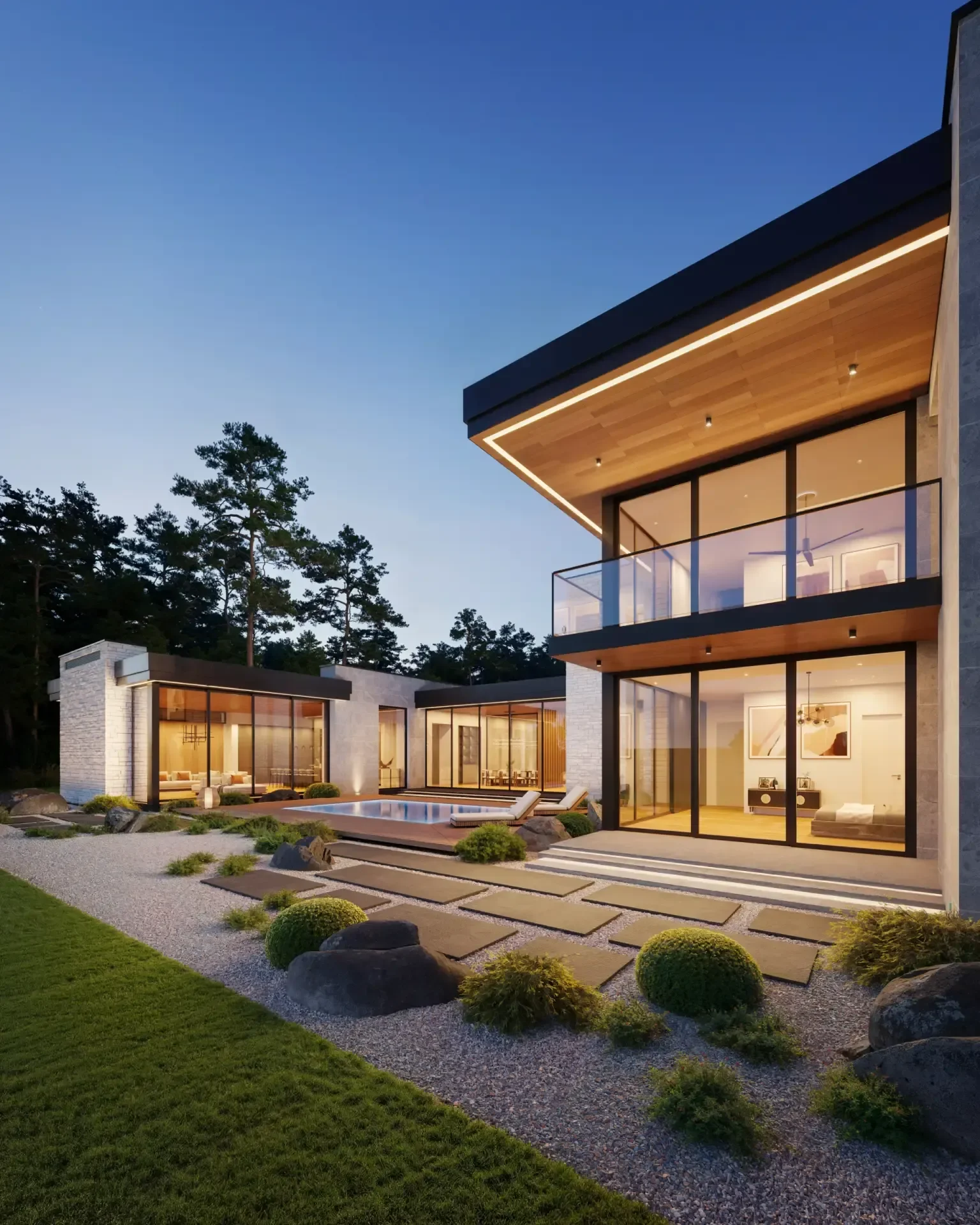 A modern house with large glass windows and wooden accents, illuminated at dusk, landscaped yard with rocks, plants, and a small pool.