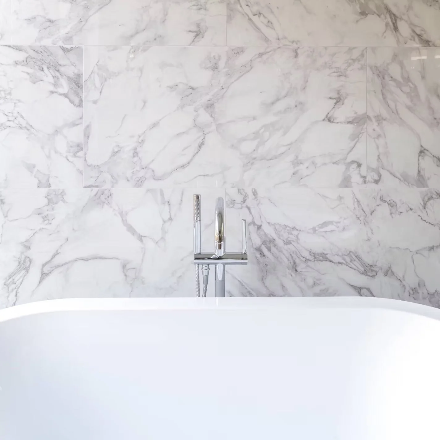 A modern bathtub with a marble wall and a chrome faucet.