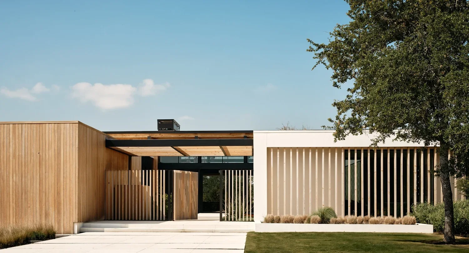 Modern building with wooden slat facade, white and black accents, and surrounding greenery.