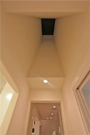 Looking up a tall, narrow indoor space with a light at the bottom and a dark opening at the top, possibly a chimney or vent shaft.
