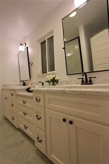 Bathroom with white cabinetry, two mirrors, and a double sink countertop with a flower arrangement in the center.