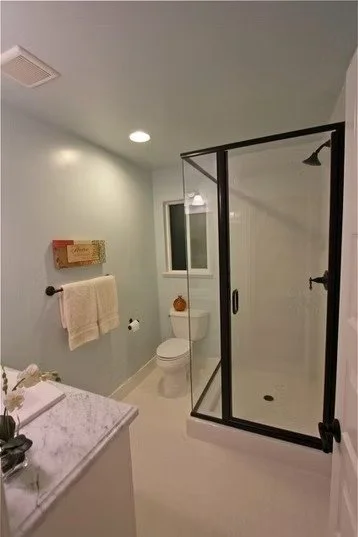 Bathroom with shower enclosure, toilet, mirror, towel rack, and vanity with marble countertop.