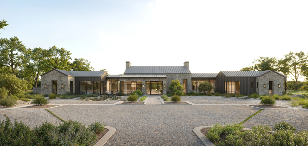Modern single-story house with stone and black exterior, surrounded by a gravel driveway, shrubs, and trees, under a clear sky.