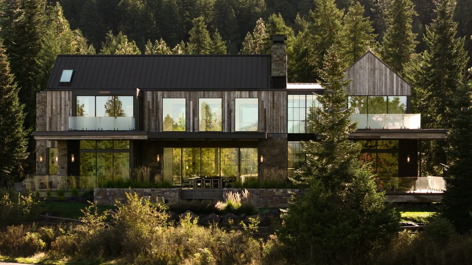 Modern multi-story house surrounded by trees with large glass windows and outdoor balcony spaces.