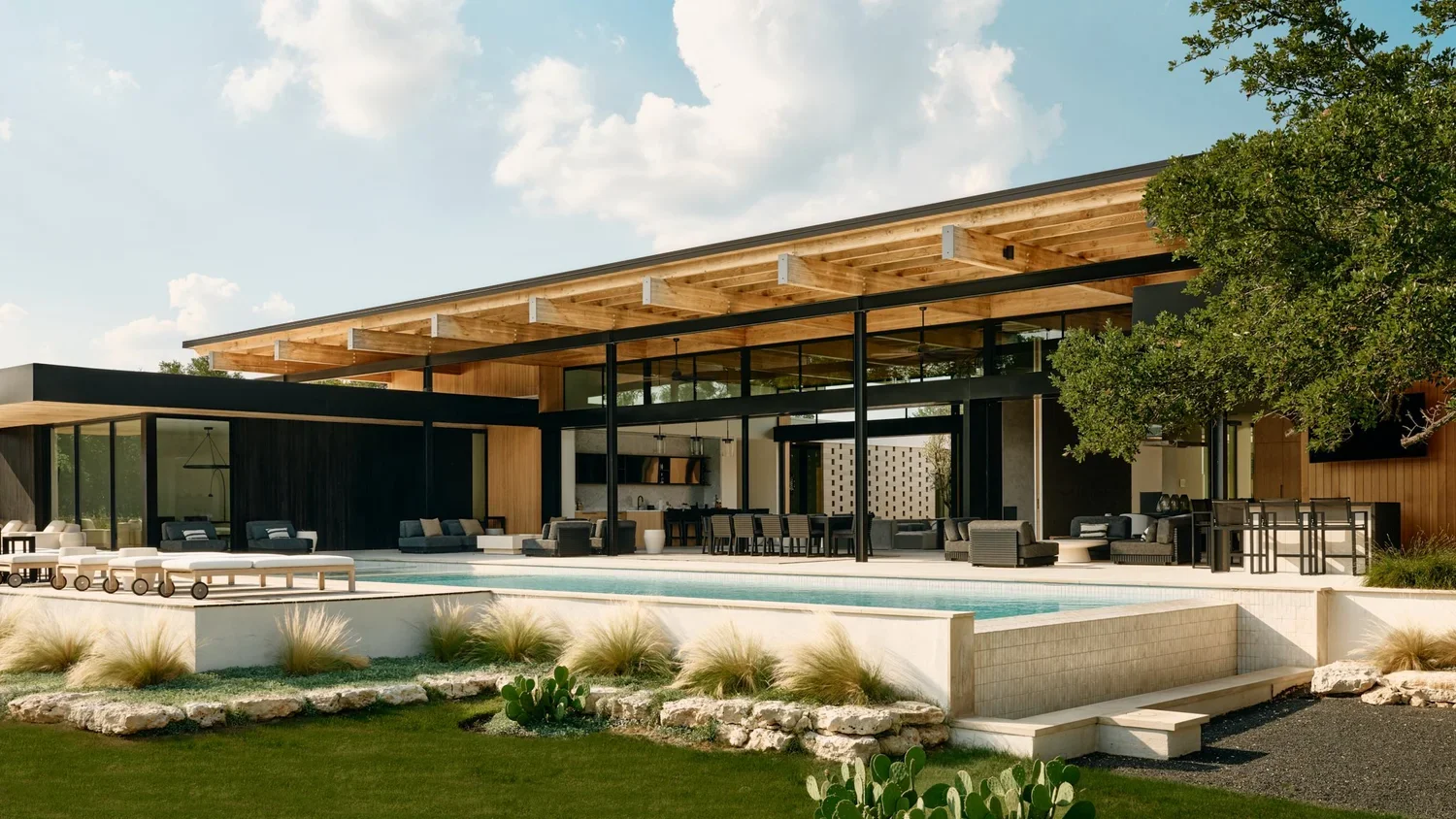 Modern house with large glass windows, outdoor seating, and a pool in a landscaped yard with desert plants and a tree.