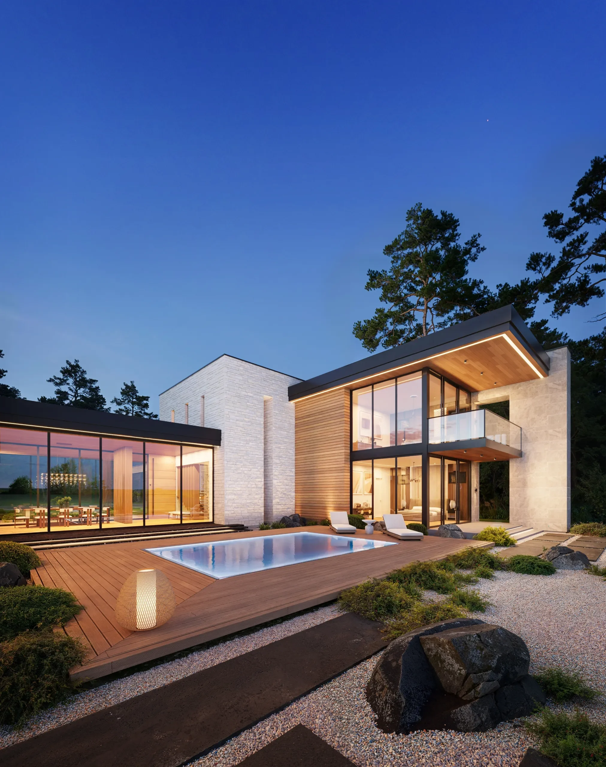 Modern house with large glass windows and balcony, surrounded by trees, with a pool and patio area with lounge chairs and decorative lighting at dusk.