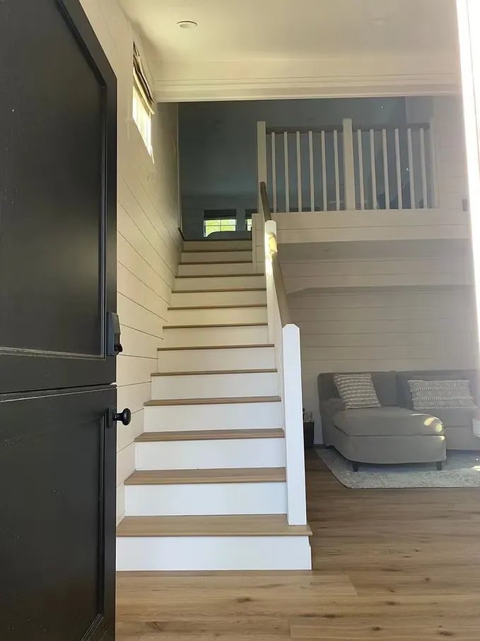 Interior view of a modern home with a staircase leading to a second floor and a partial view of a gray couch with pillows.