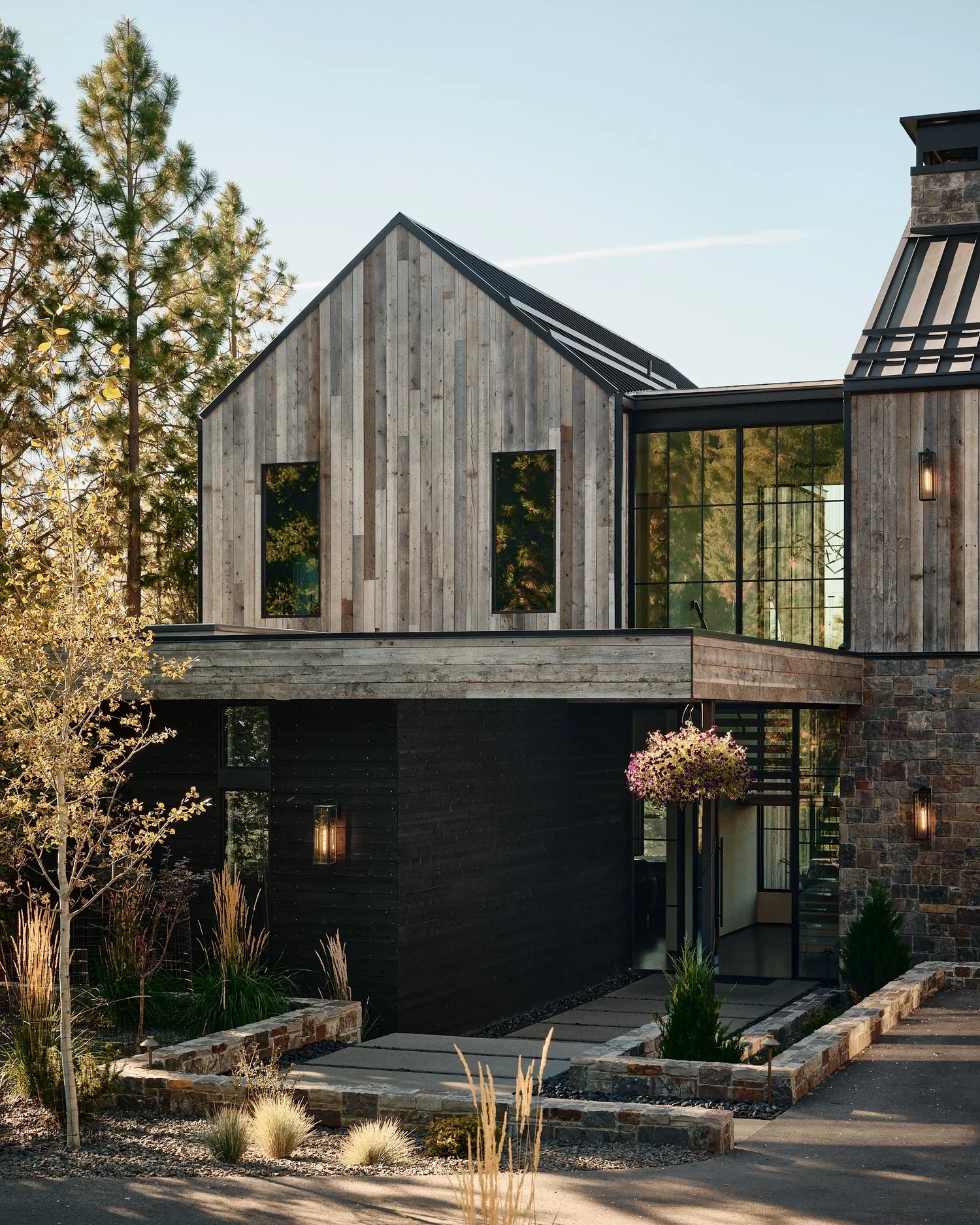 Modern house with wooden and black exterior, large glass windows, and a landscaped front yard with plants and a pathway.