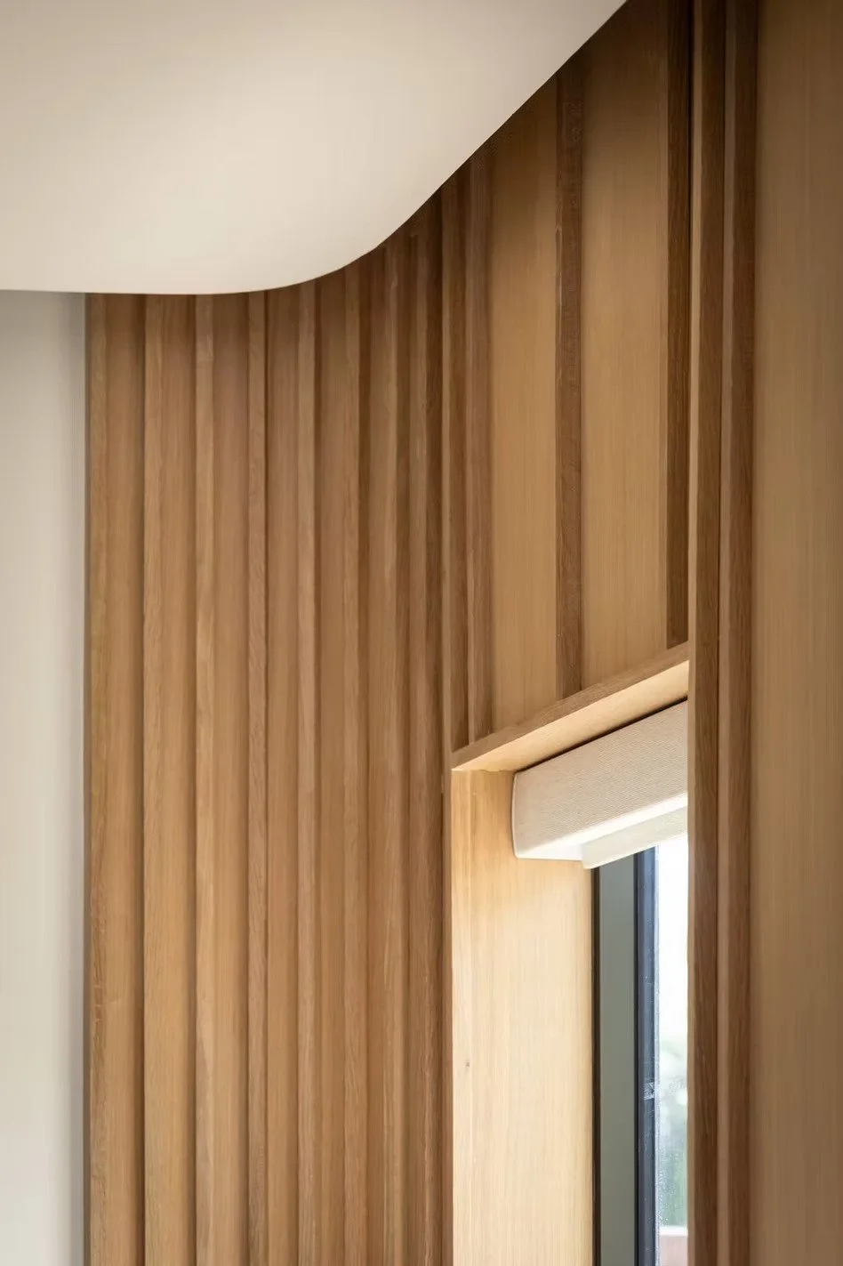 Interior view of a wooden ceiling with vertical wooden slats and a window with a fabric blind.
