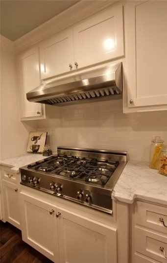 Kitchen with white cabinets, marble countertops, and a stainless steel stove and range hood.