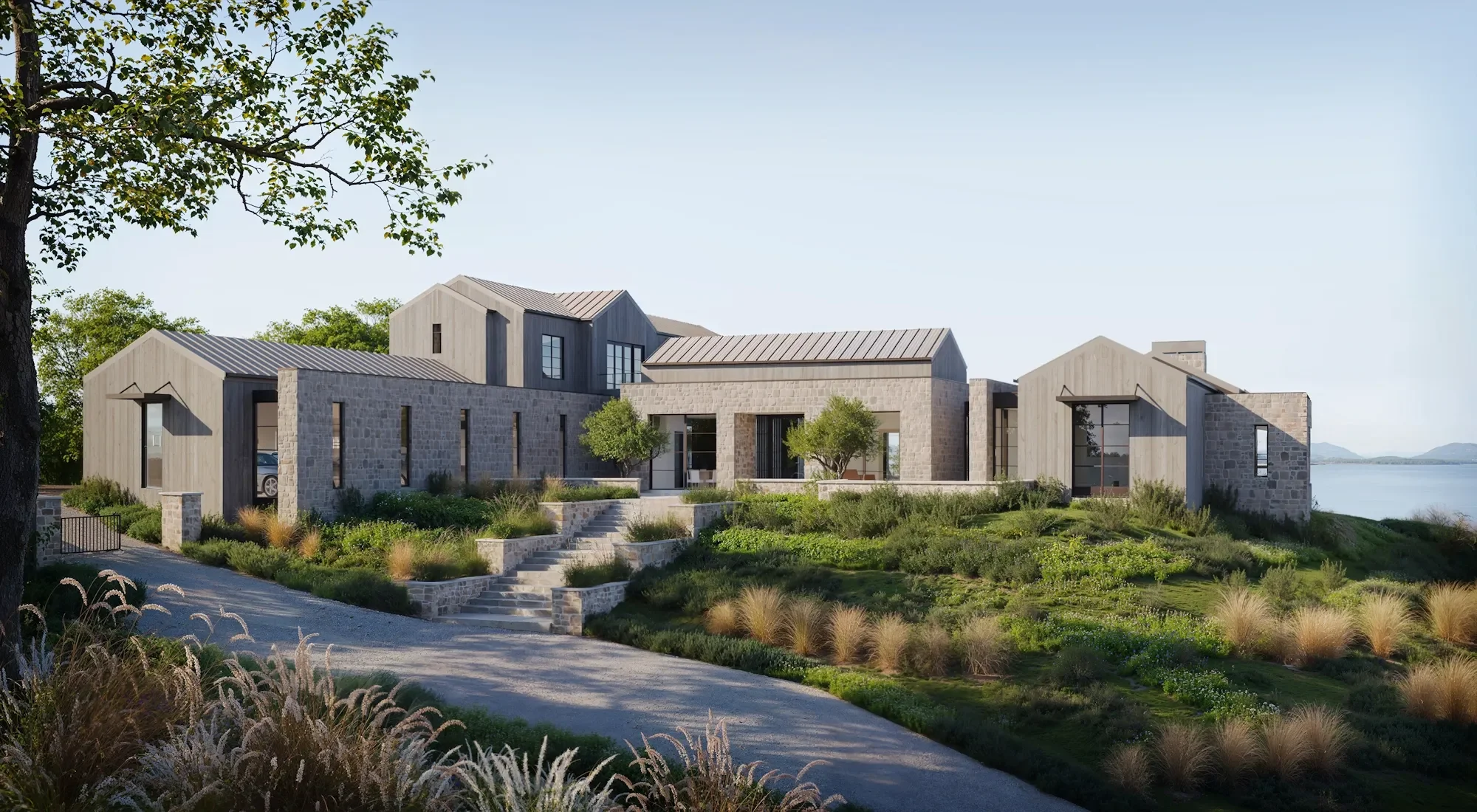 Modern house with stone and wood exterior, located near water with landscaped garden and staircase leading to entrance.