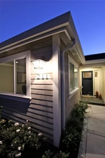 Close-up of the corner of a house with house number 221 and a porch light at dusk.