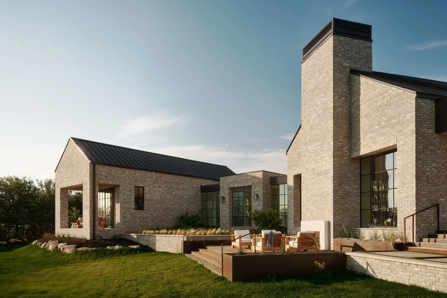 Modern house with brick exterior, large windows, and a patio with outdoor seating on a grassy lawn under a clear sky.