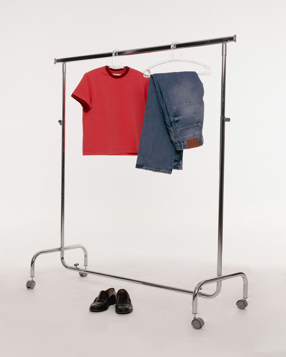 Clothing rack with a red t-shirt and blue jeans hanging on hangers, and black shoes on the floor below.