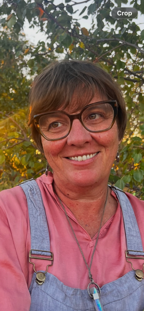 Kate Shannon with short brown hair, glasses, and a pink shirt, smiling outdoors with trees in the background.