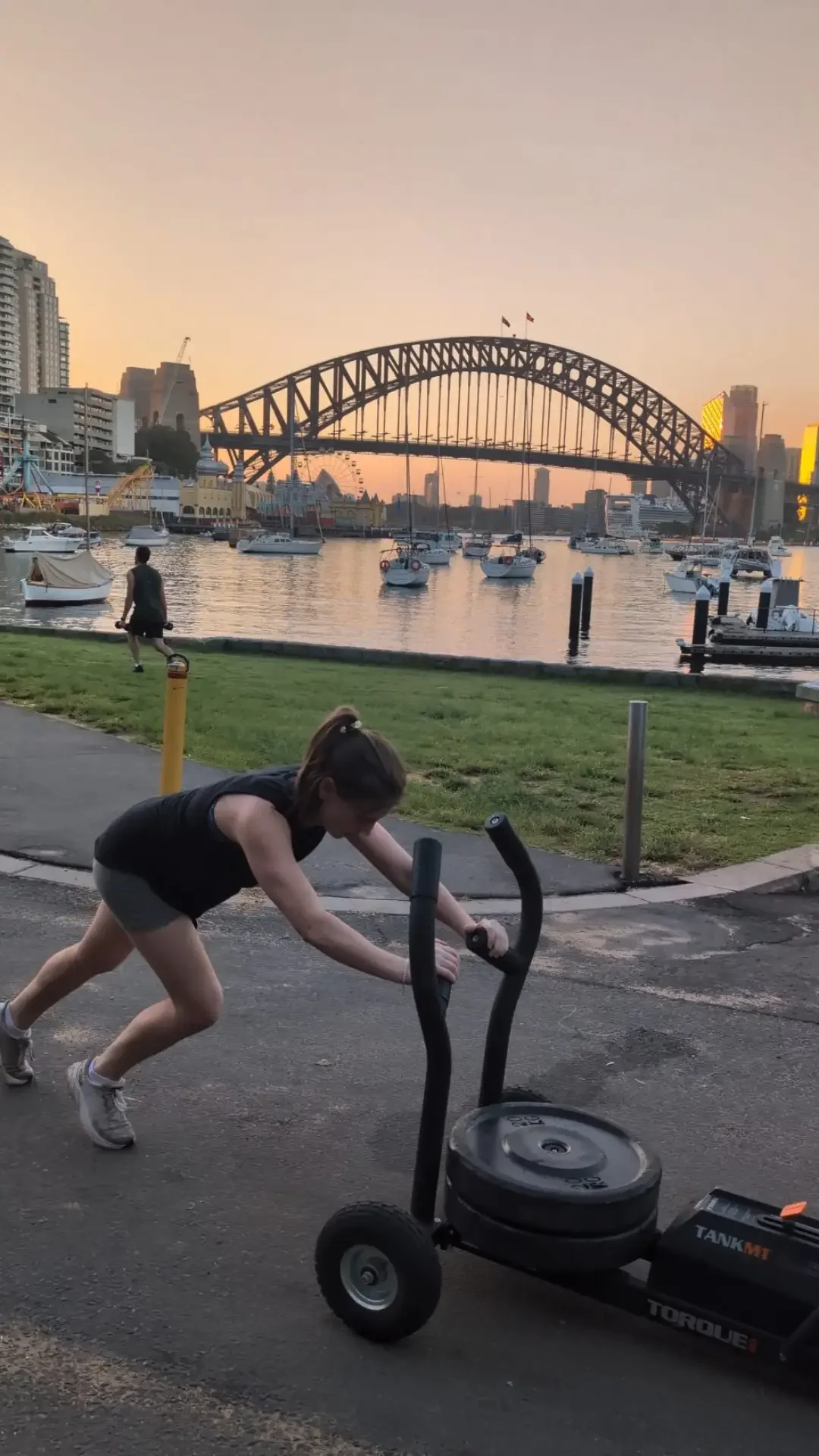 woman pushing sled in burn hyrox class at lavender bay with harbour bridge in background