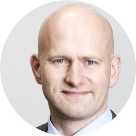 Et portrætfoto af en smilende, skaldet mand i en forretningsdragt mod en lys baggrund.