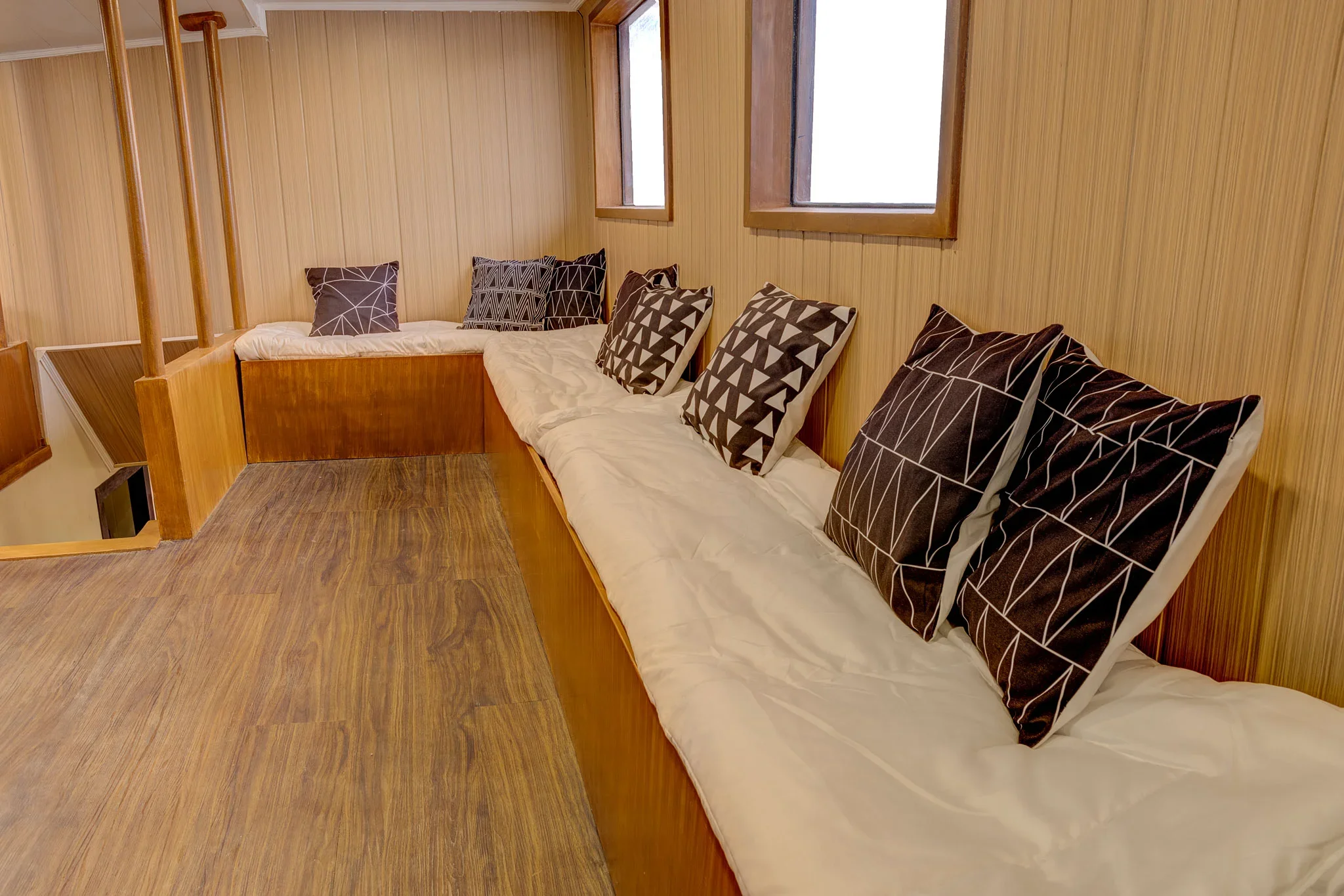 Wood-paneled sitting area with patterned pillows, small windows, and a wooden floor.