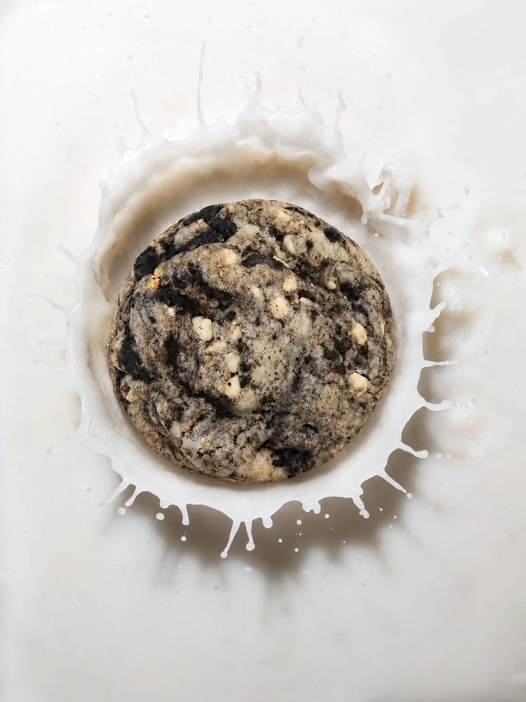 Cookies with black and white chocolate chips in a splash of milk on a white background.