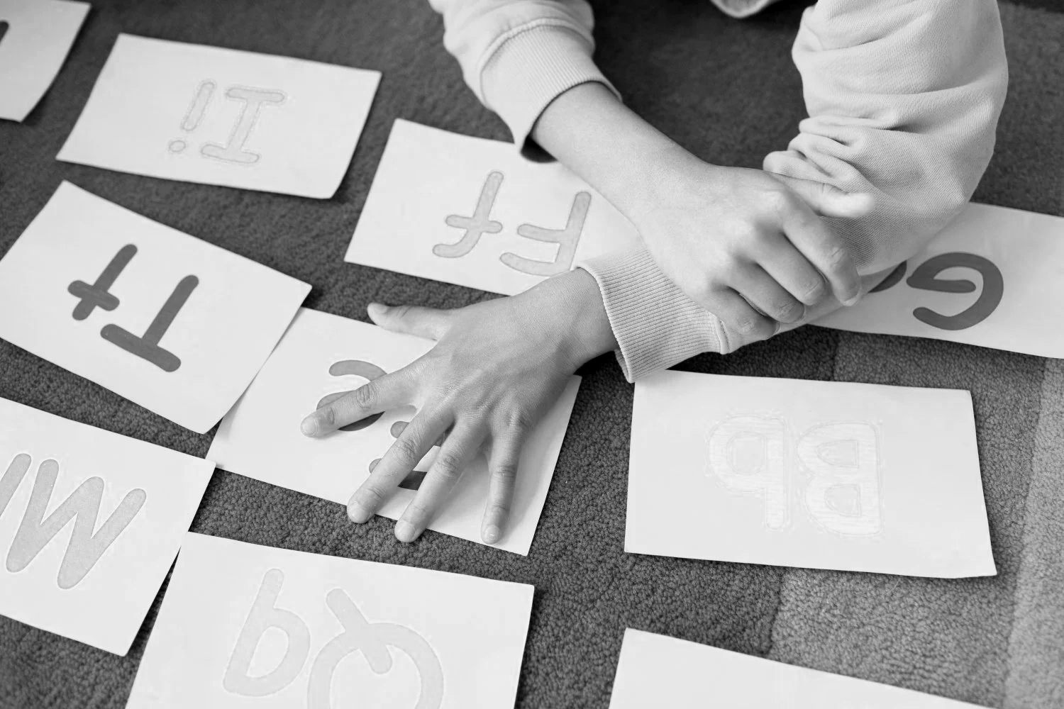 Child working on letter recognition with alphabet flashcards on a carpeted floor, black and white photograph.