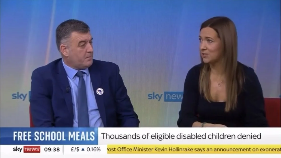 Natalie Hay on a Sky News broadcast. The man is wearing a dark suit and a blue shirt, and Natalie is wearing a black top. The lower third of the screen shows headlines about free school meals and disabled children