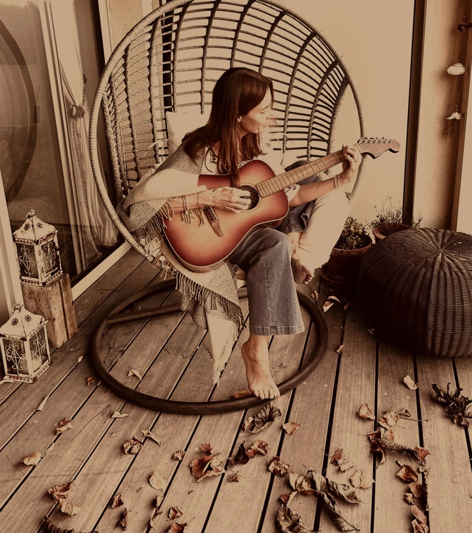 Woman sitting in a hanging chair playing guitar on a porch decorated with autumn leaves and lanterns.