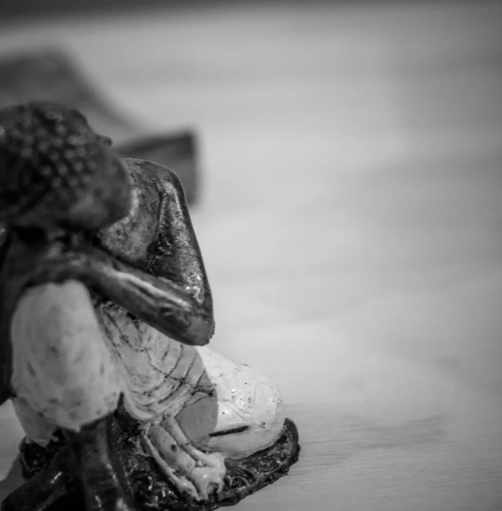 Close-up of a small decorative figurine of a person sitting, made of a shiny material, placed on a wooden surface with a blurred background.