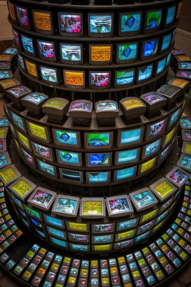 A large circular display of multiple old CRT televisions arranged in concentric rings showing colorful images and videos.