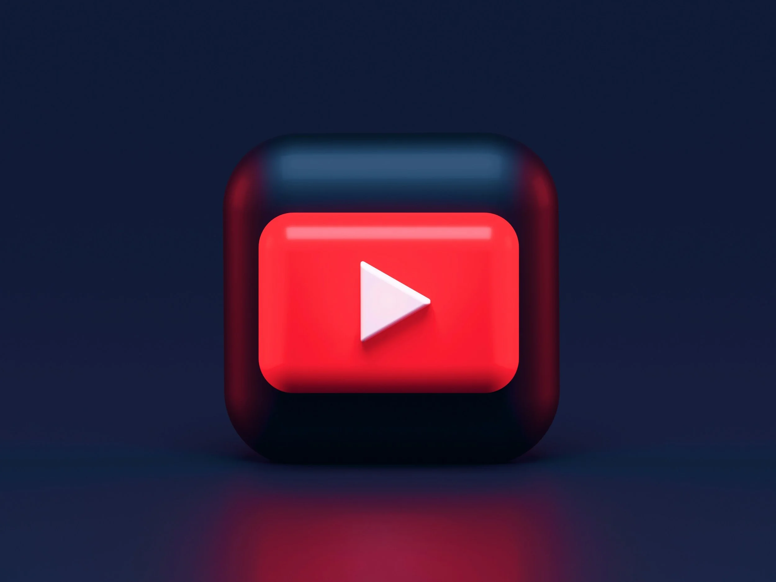 3D icon of a YouTube play button with a white triangle on a red background, set on a dark background.