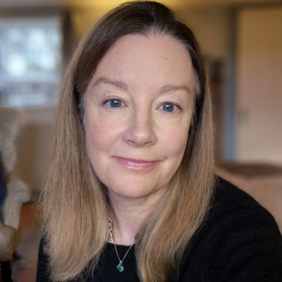 A counsellor with long brown hair and blue eyes smiling in a cosy indoor setting.