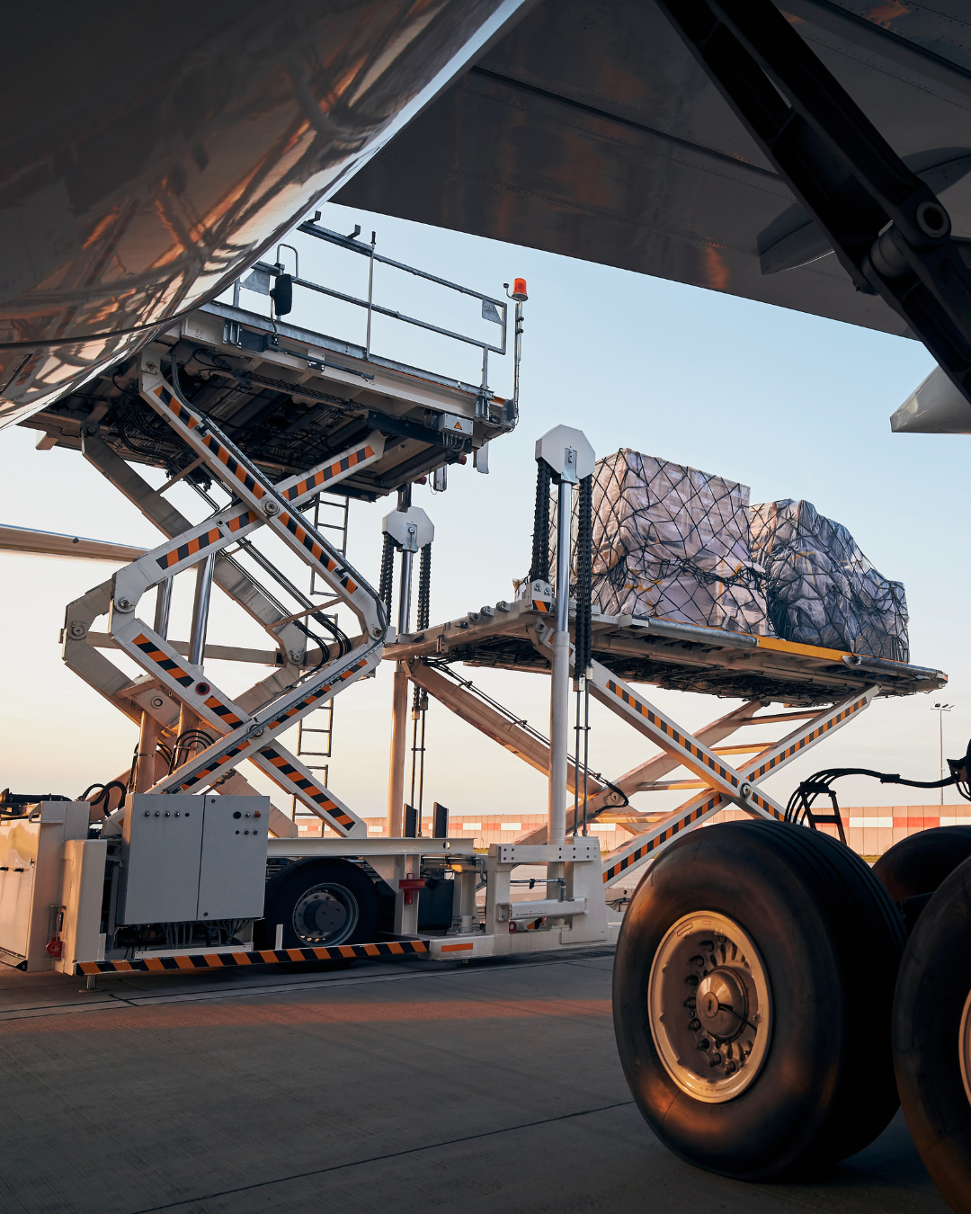 Transportfordon med höj- och sänkbara plattformar som lastar stora paket eller bagage på en flygplats.