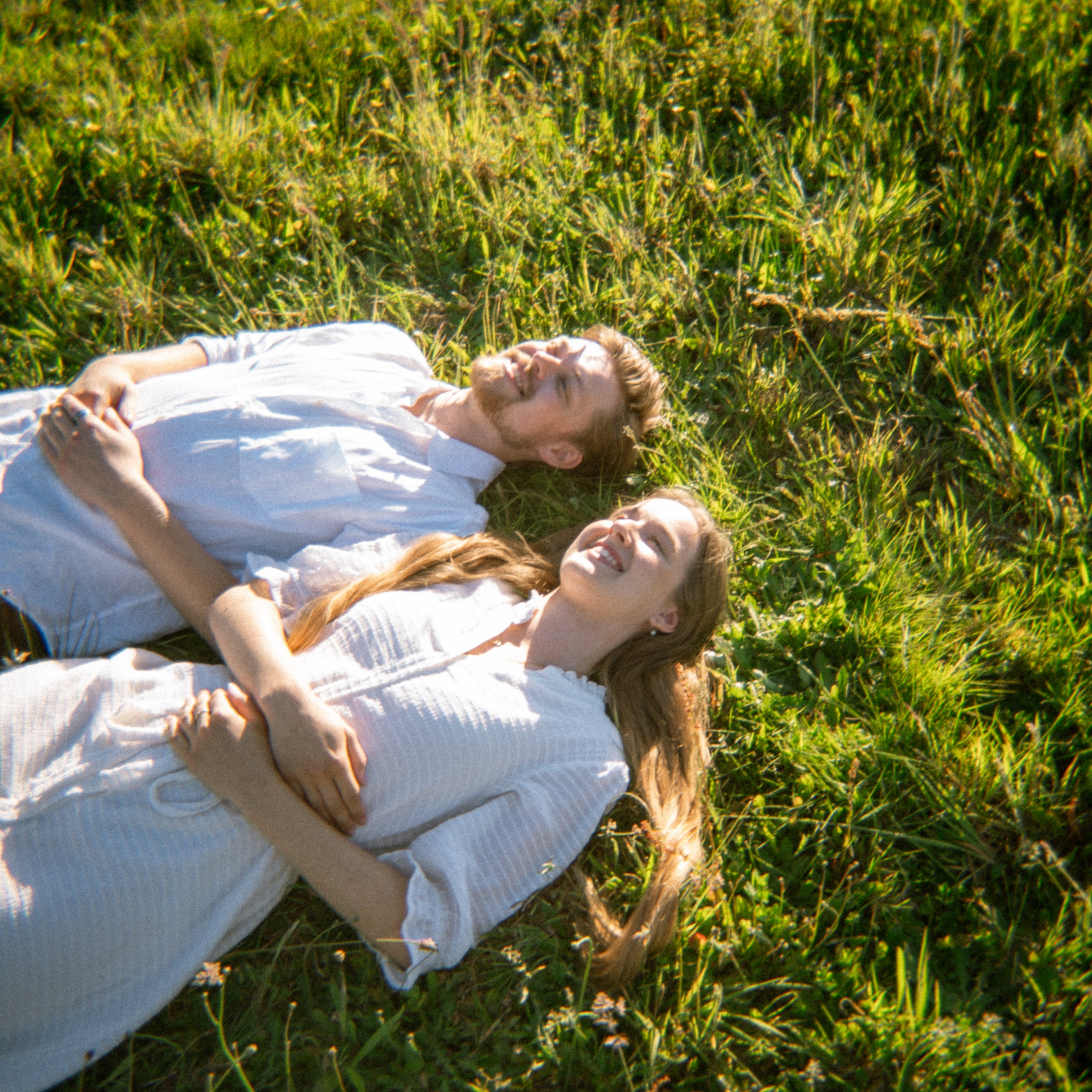 Portret van man en vrouw liggen in een weiland met groen gras en bloemen, genieten van de zon.