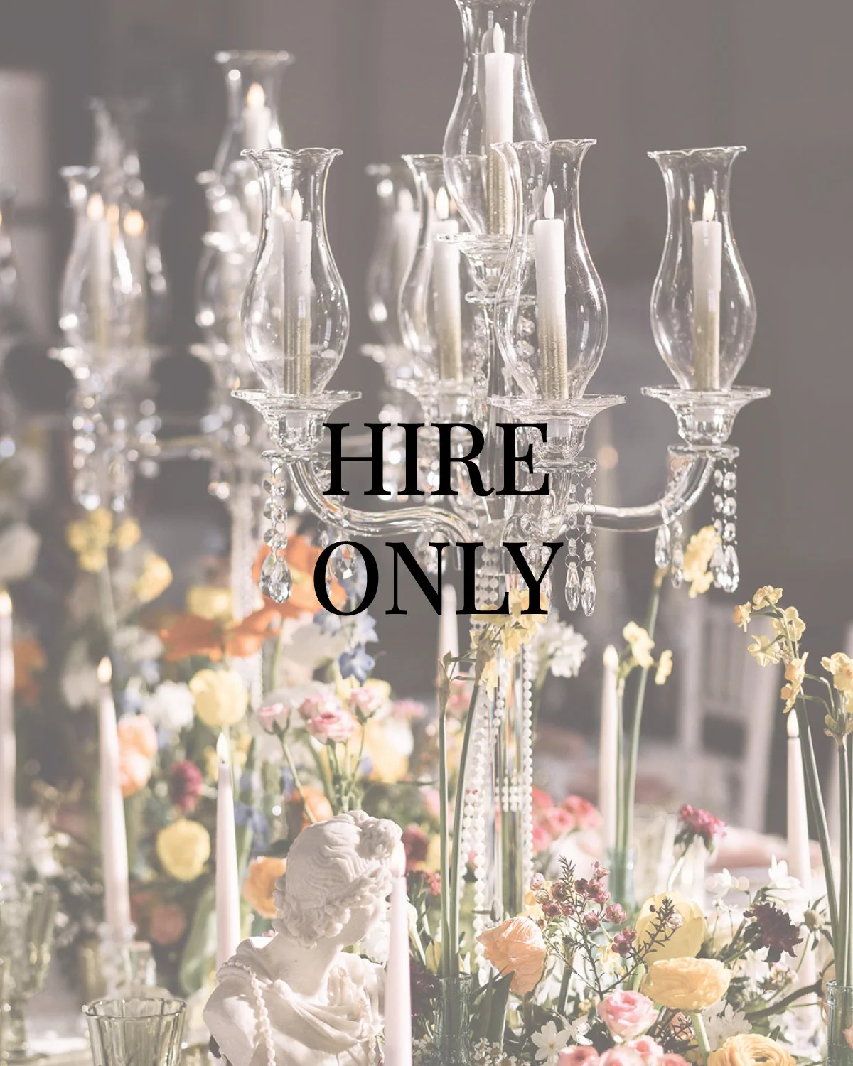 A luxurious chandelier with white candles hangs above a table decorated with flowers and a small cherub statue.
