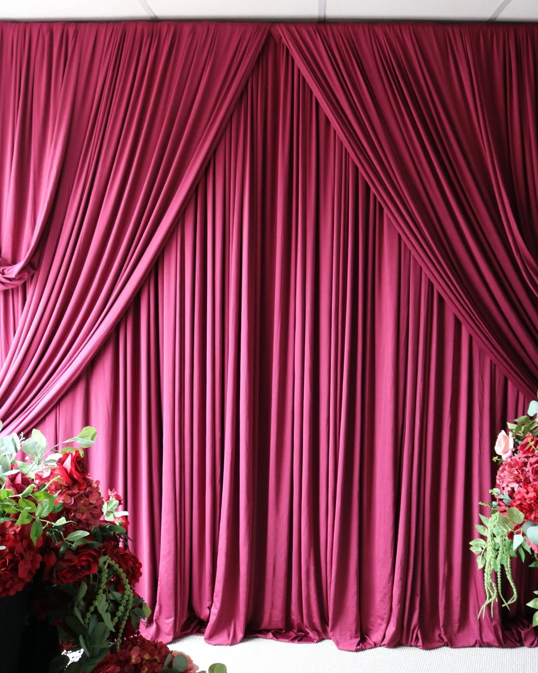 Burgundy drapery installation with floral arrangements on both sides.