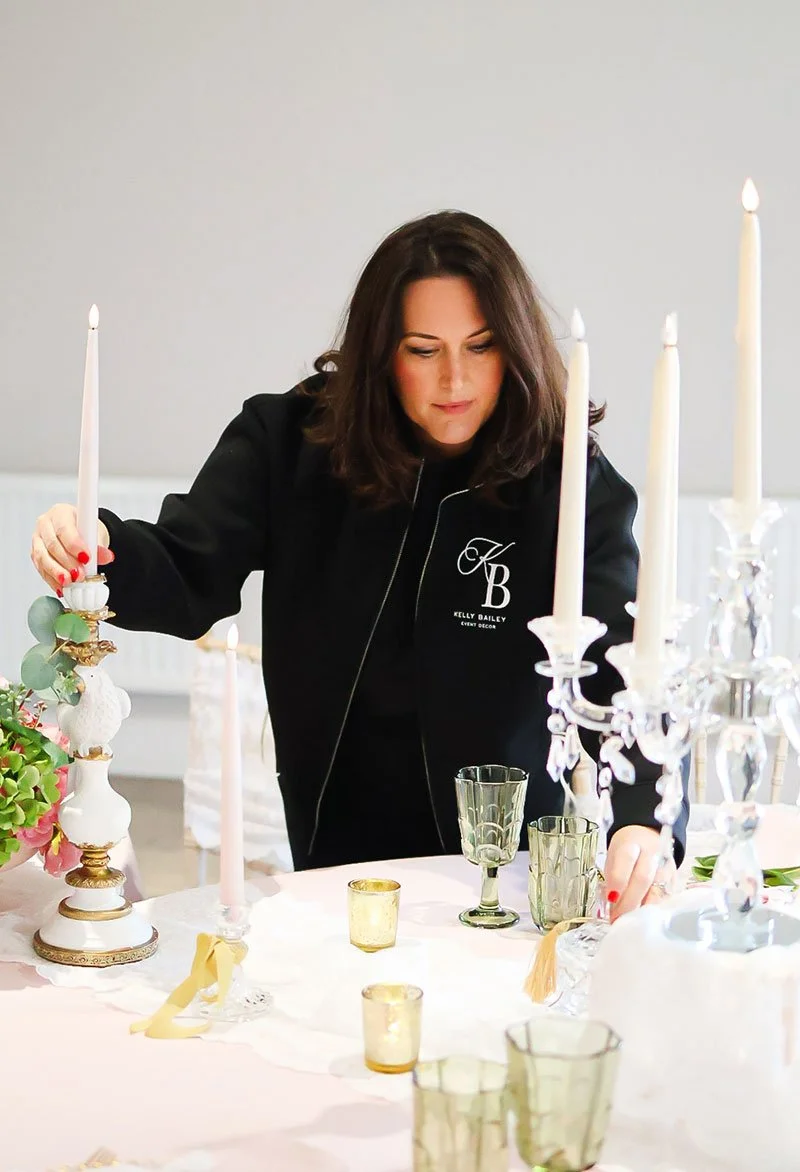 Woman arranging a decorated table with candles and glassware for an event.