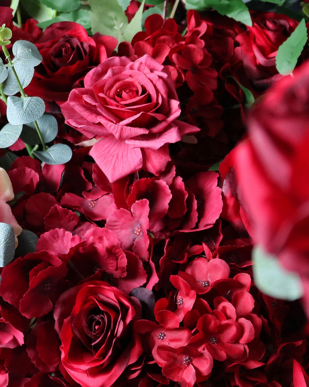 A close-up of red roses, pink flowers, and green leaves, with some flowers decorated with small rhinestones.