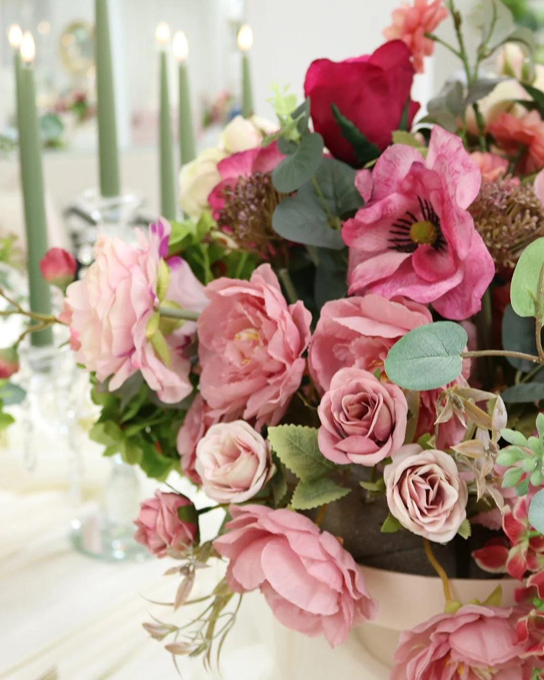 Close-up of a colorful floral arrangement with pink, red, and white flowers and green leaves, placed on a table with blurred background.