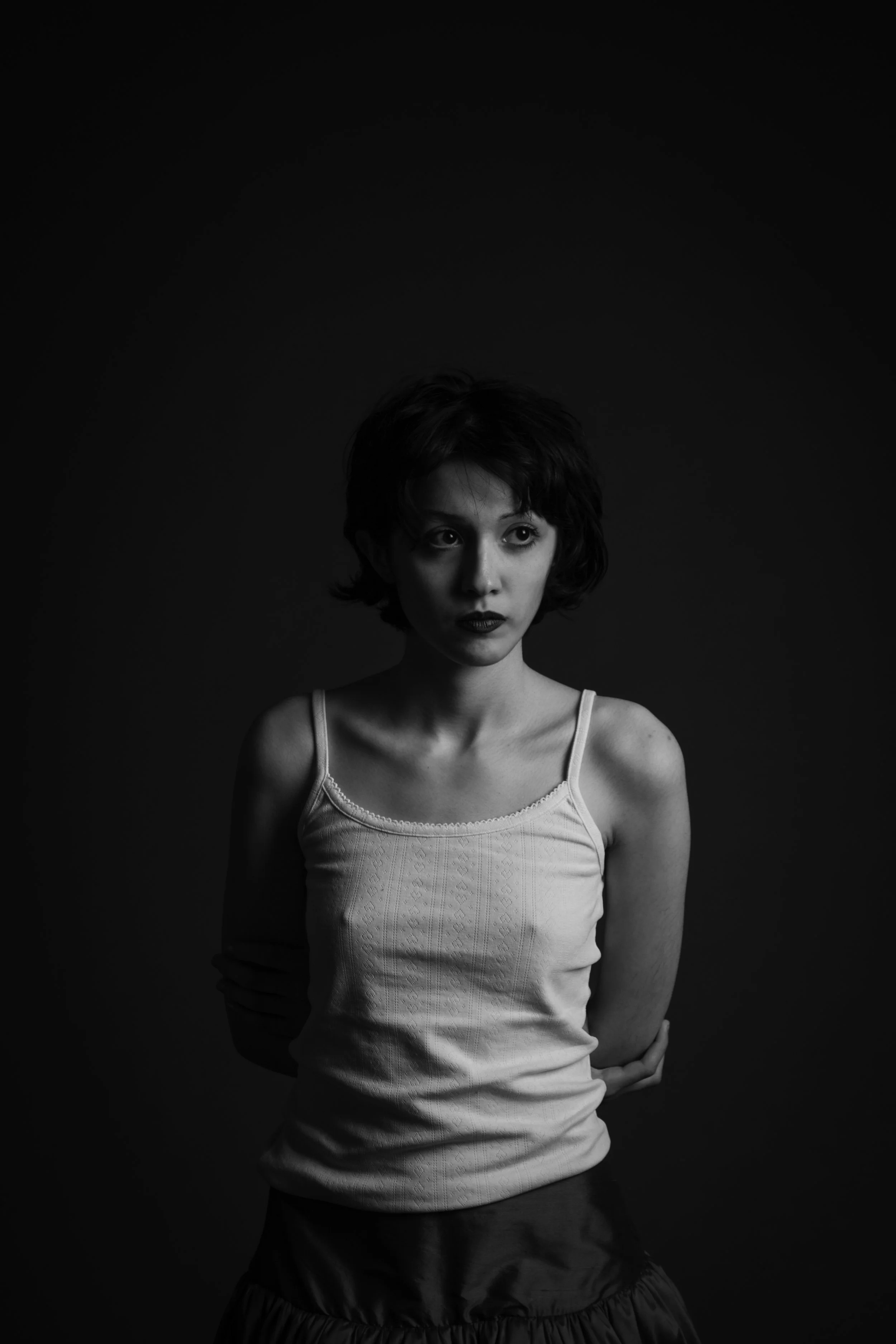Black and white portrait of a young woman with short curly hair, wearing a spaghetti strap top and a skirt, looking to the side with a serious expression.