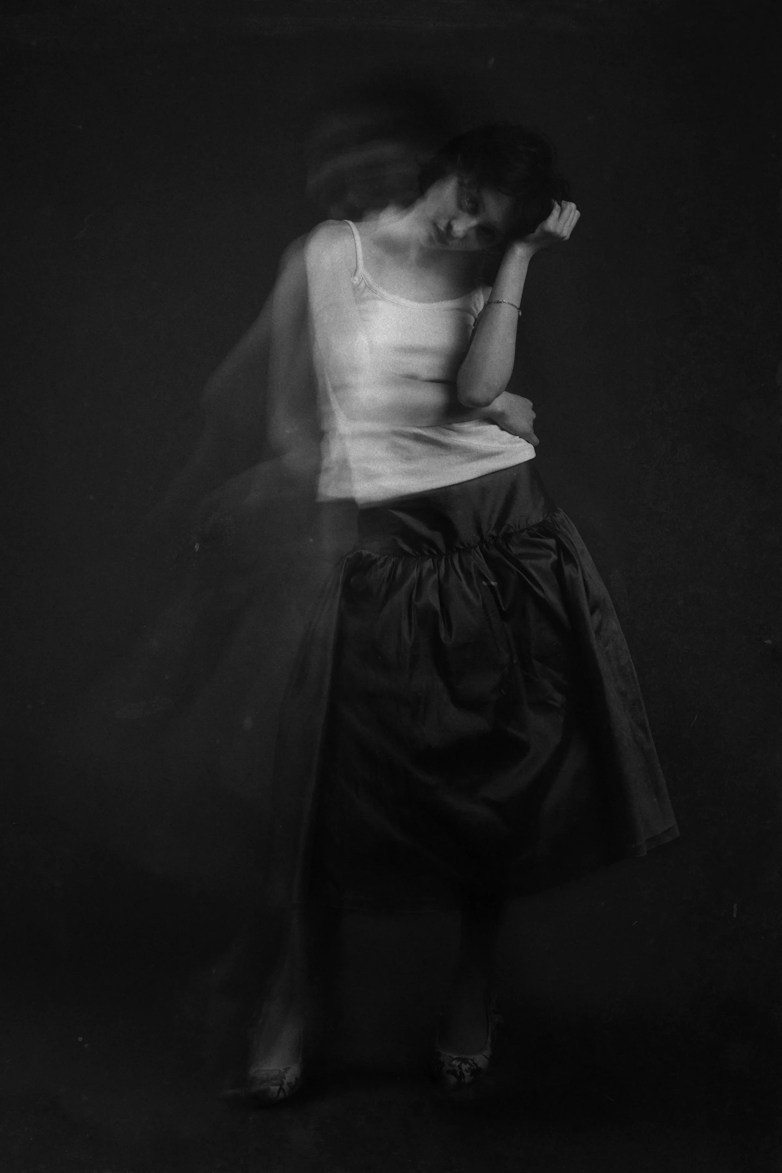 Black and white photograph of a woman in motion, wearing a sleeveless top and a long skirt, with blurred movement around her, creating a ghostly effect.