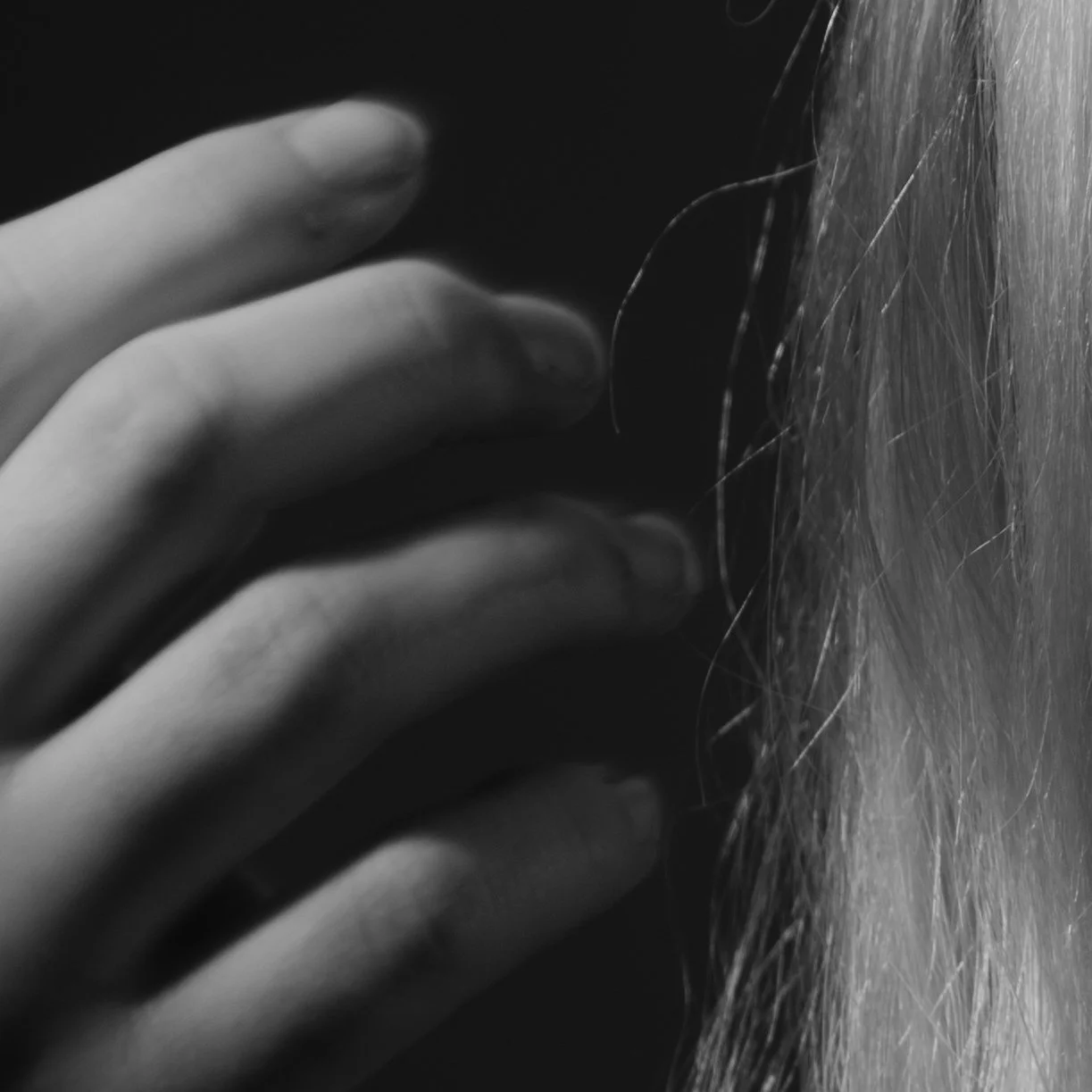 Close-up of a hand touching a person's ear and hair in black and white.