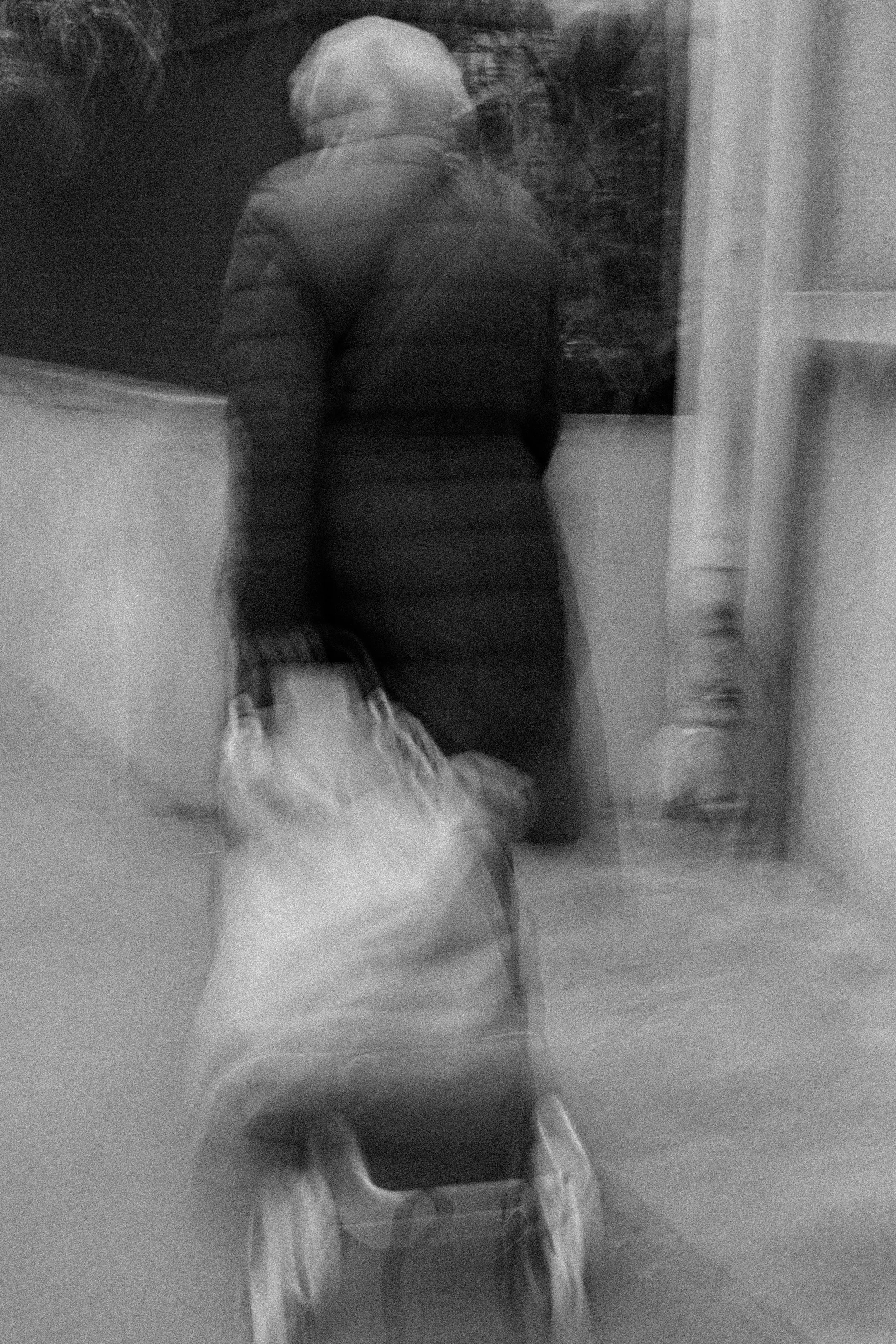 A person in a winter coat carrying a bag, seen through a window with motion blur.