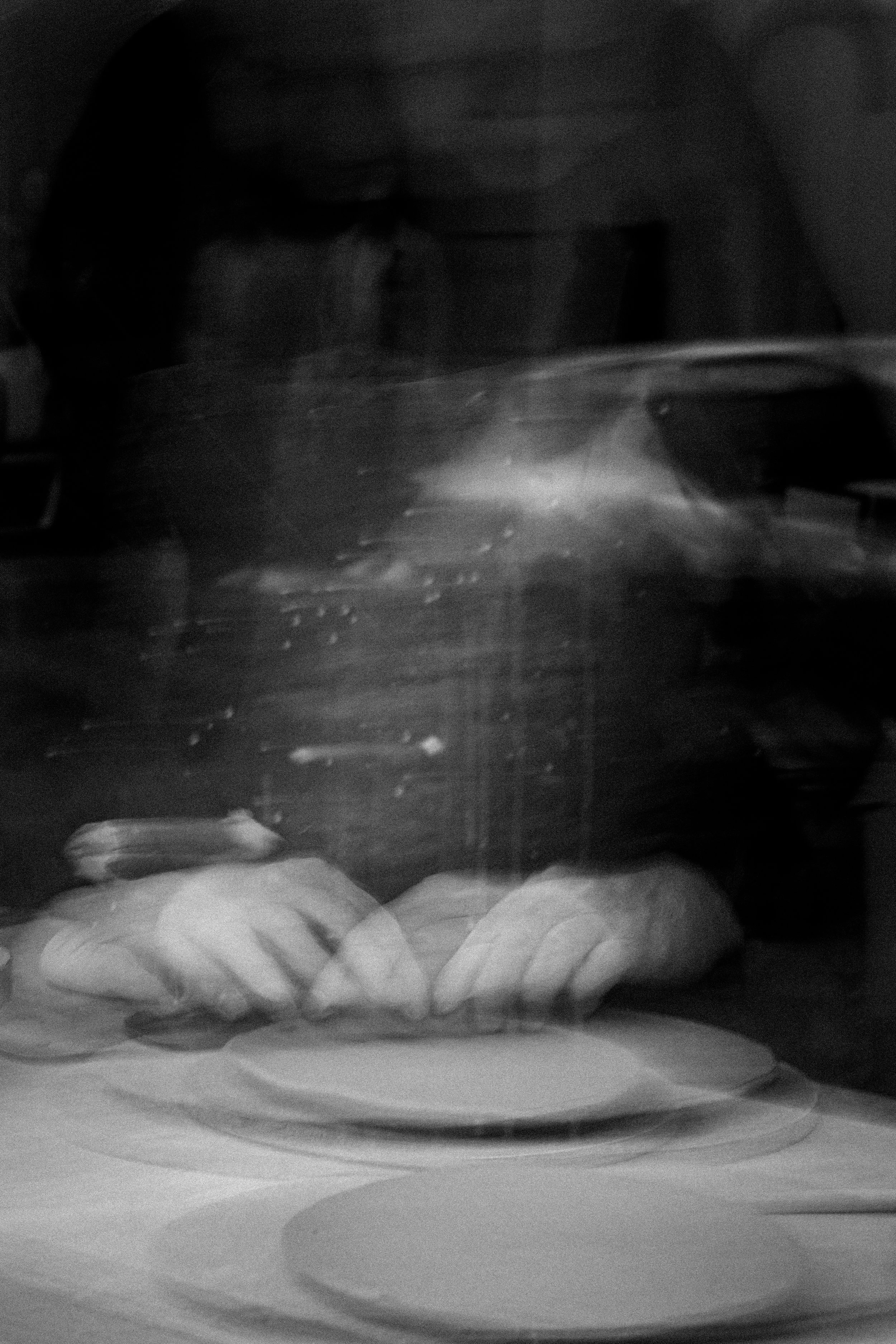 A person taking a photograph of a stack of plates and hands on a table, reflected in a mirror.