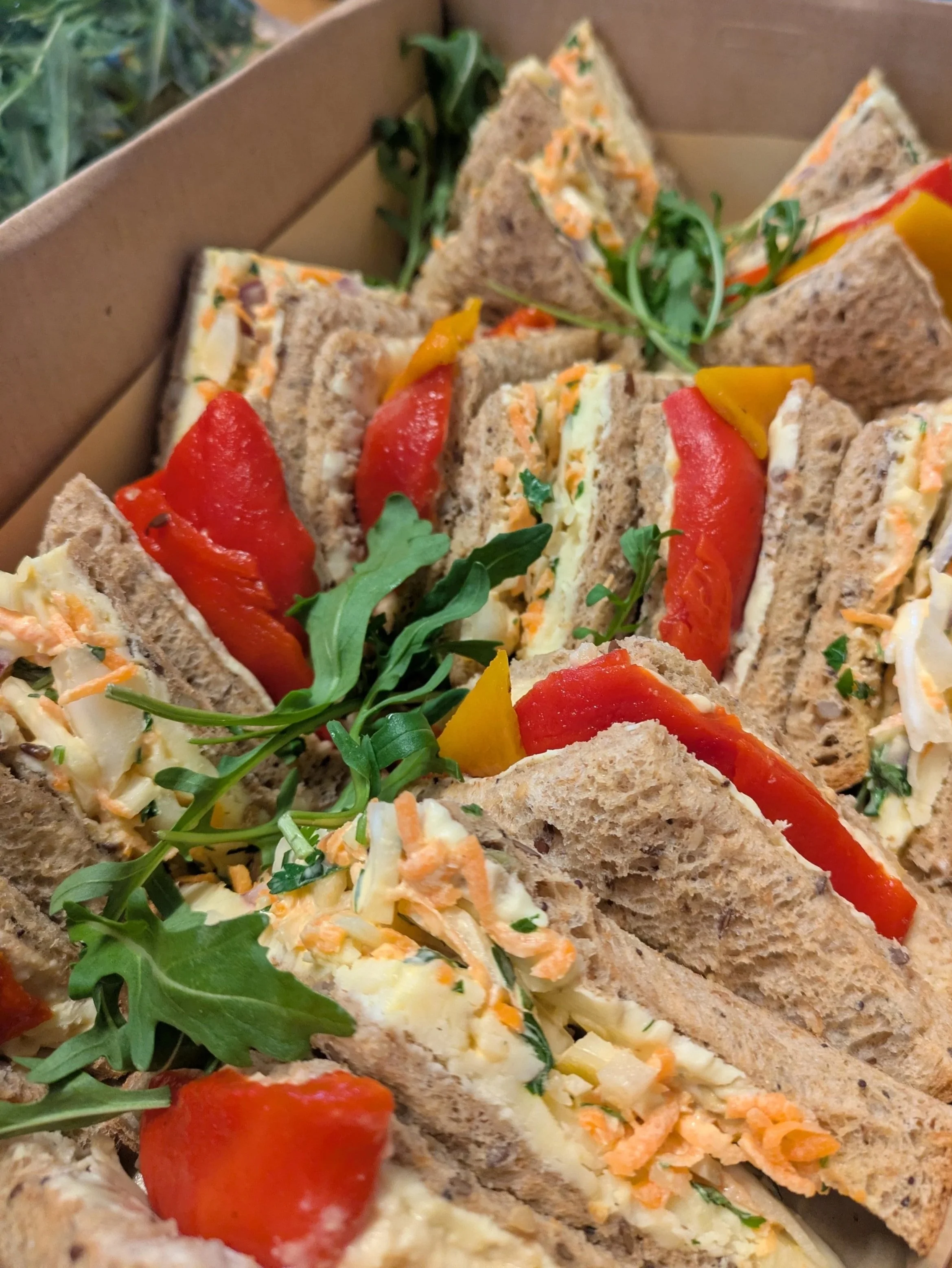 Close-up view of veggie sandwiches with red and yellow peppers, arugula, shredded carrots, and cheese on whole grain bread.