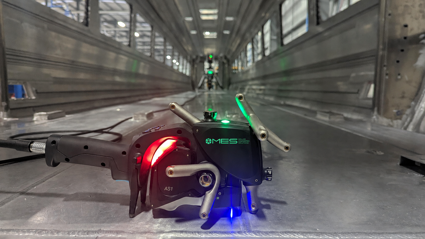 A robotic device with LED lights on a metallic surface inside a modern building or tunnel.