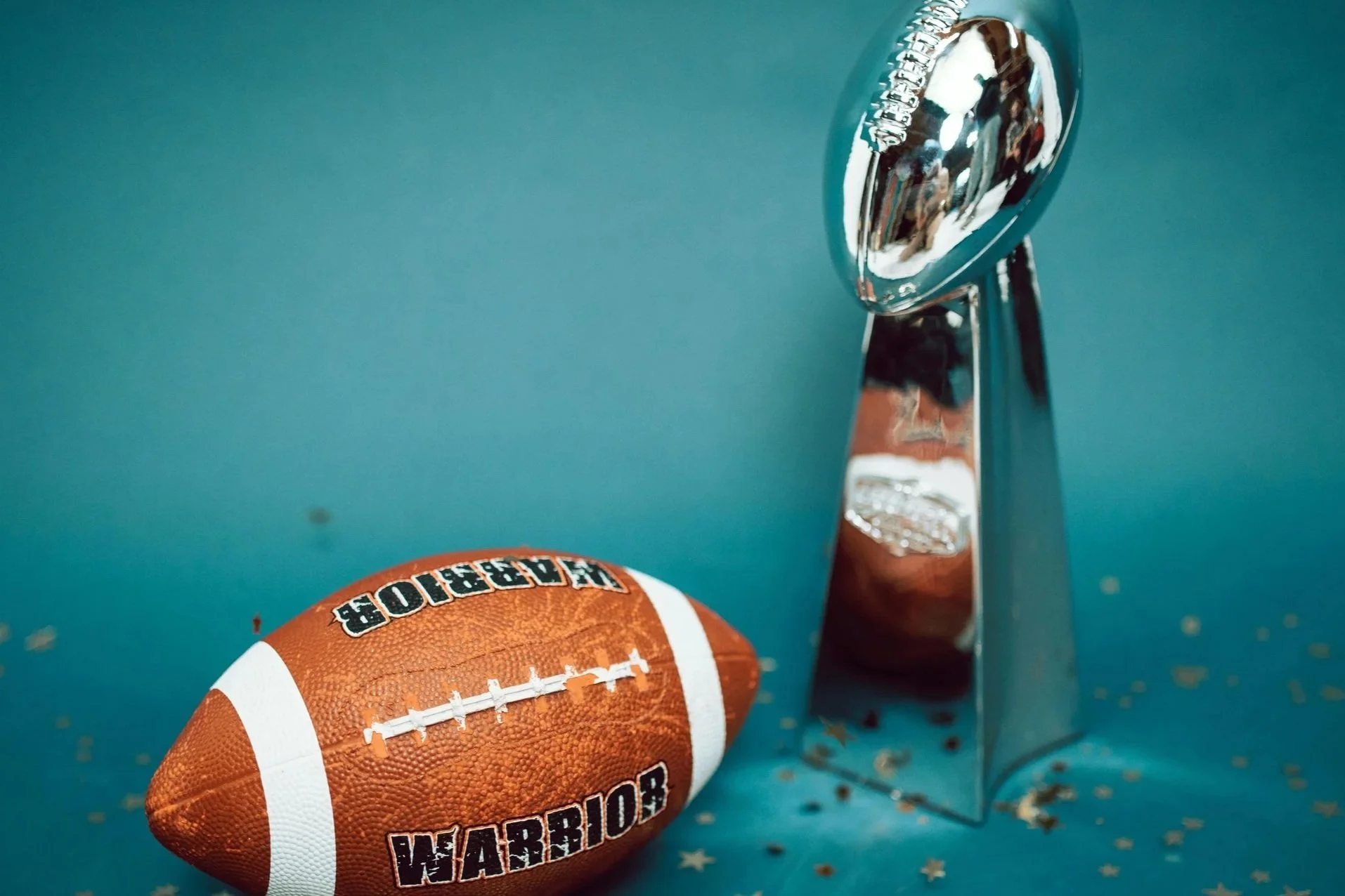Ein American Football liegt neben einem silbernen Pokal auf einer blauen Oberfläche.