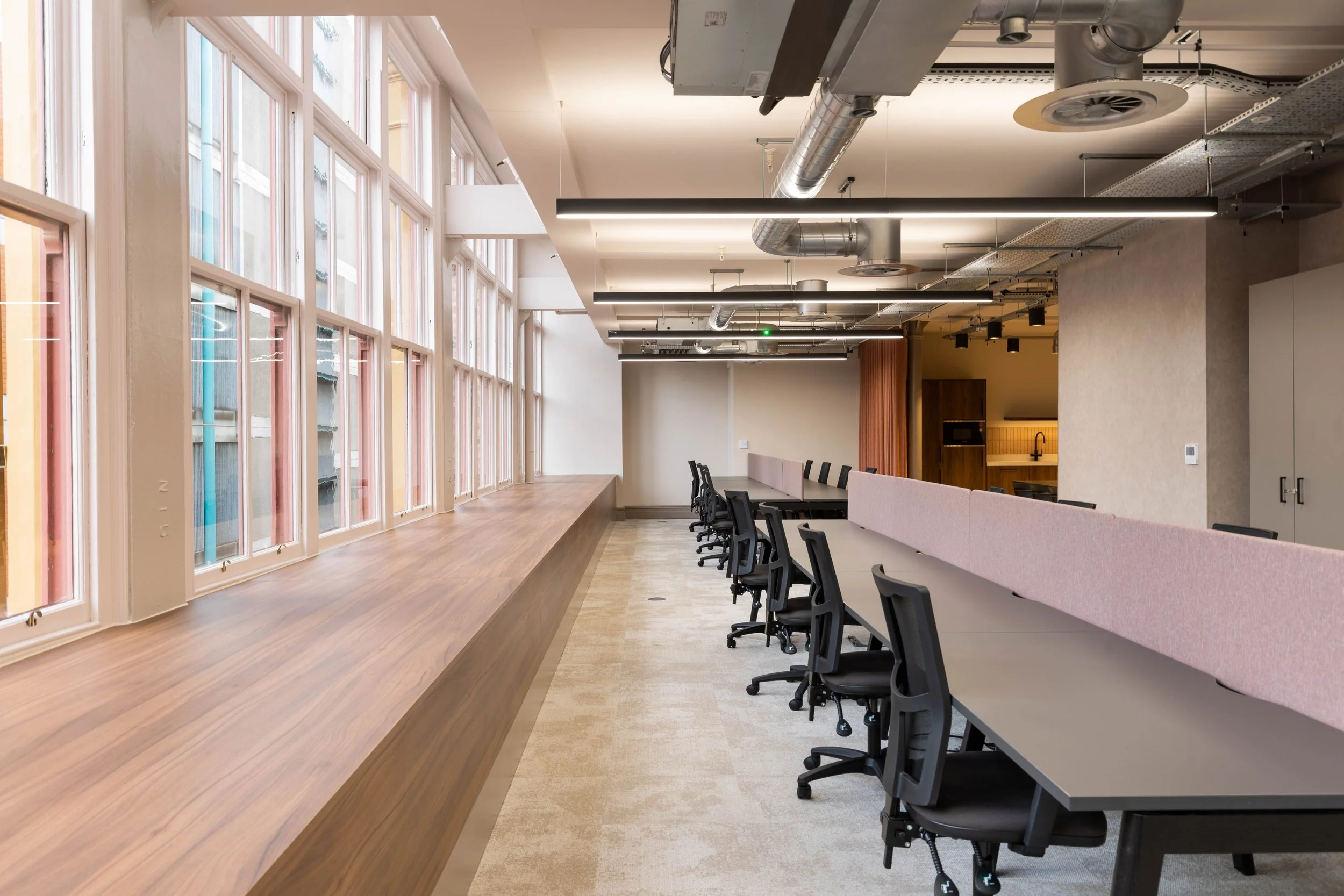 Modern conference room with long table, ergonomic chairs, large windows, and exposed ceiling ducts.