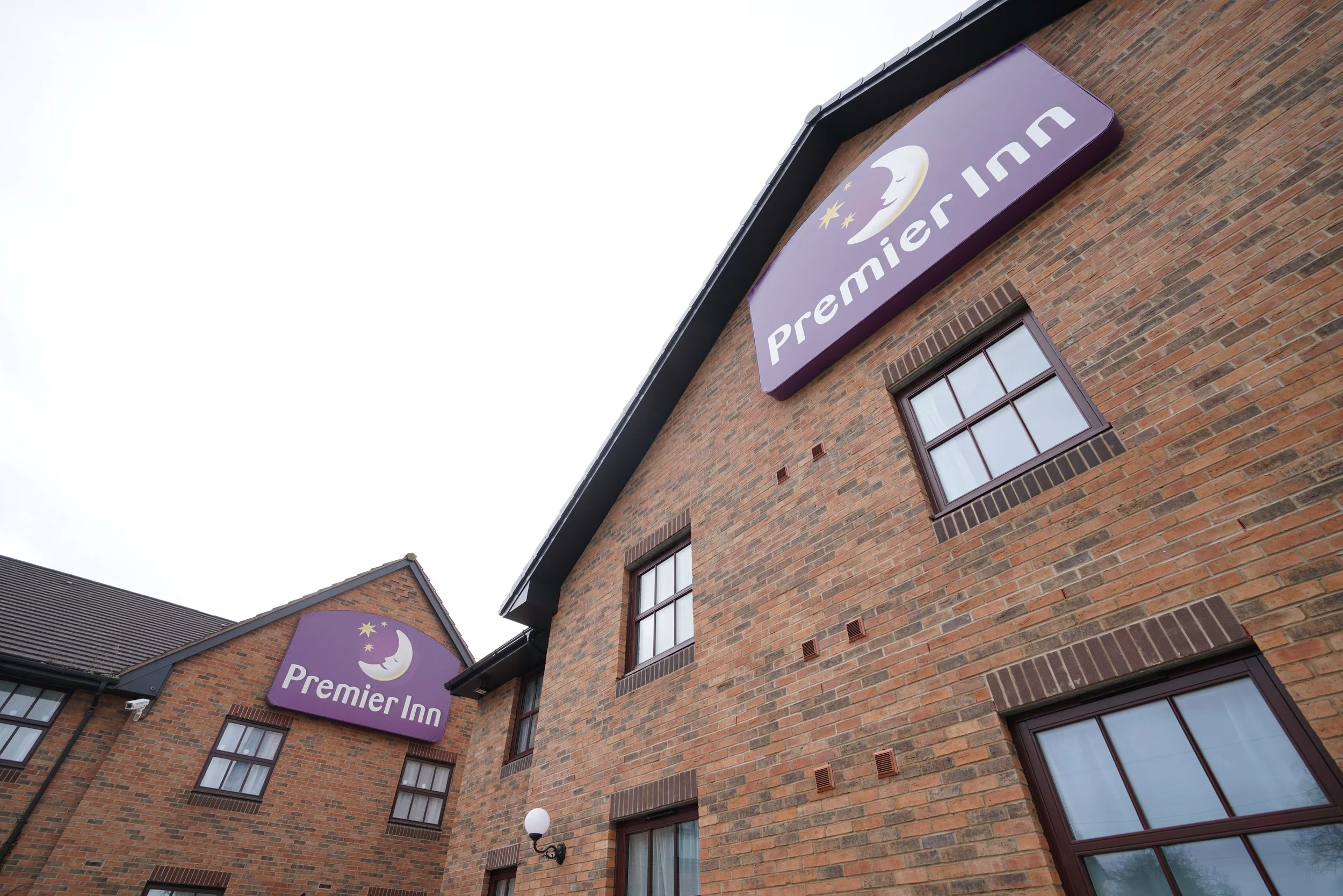 The exterior of a brick building with multiple windows and two purple signs for Premier Inn, featuring a moon and stars logo.