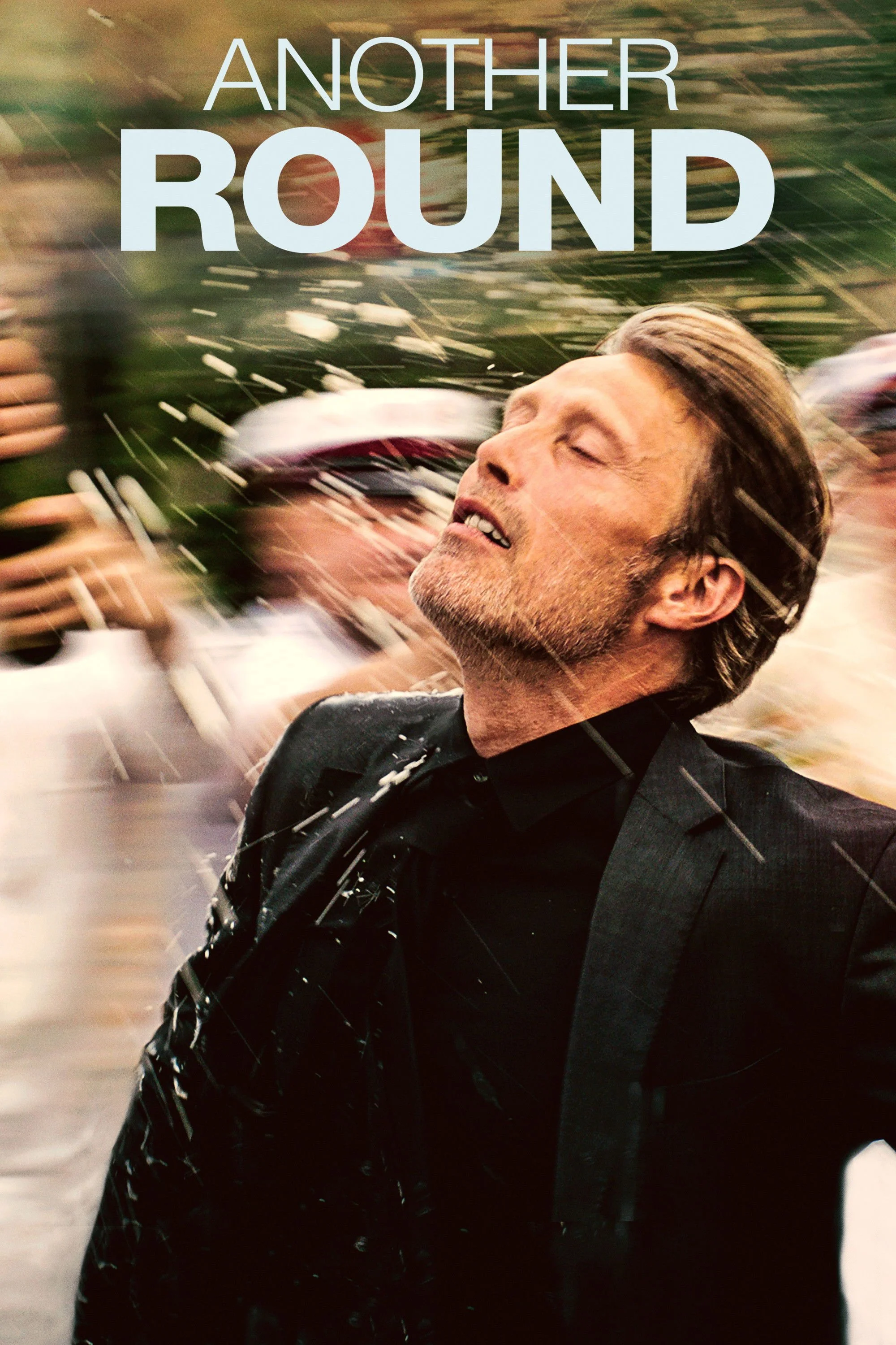 A man with short brown hair and a beard in a black suit is smiling with his eyes closed, surrounded by a movement blur. The text 'Another Round' appears at the top of the image.