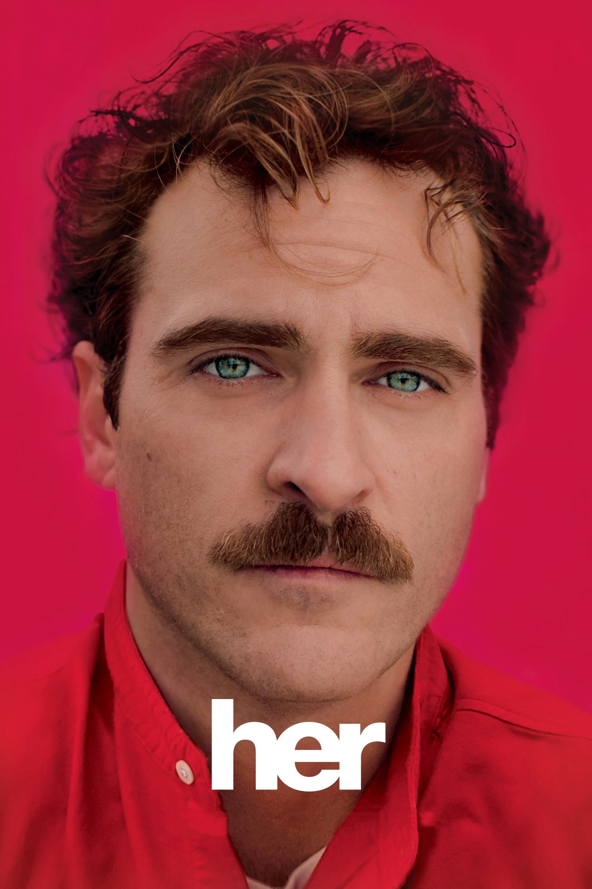 Close-up of a man with curly brown hair, blue eyes, and a beard, wearing a red shirt against a pink background.