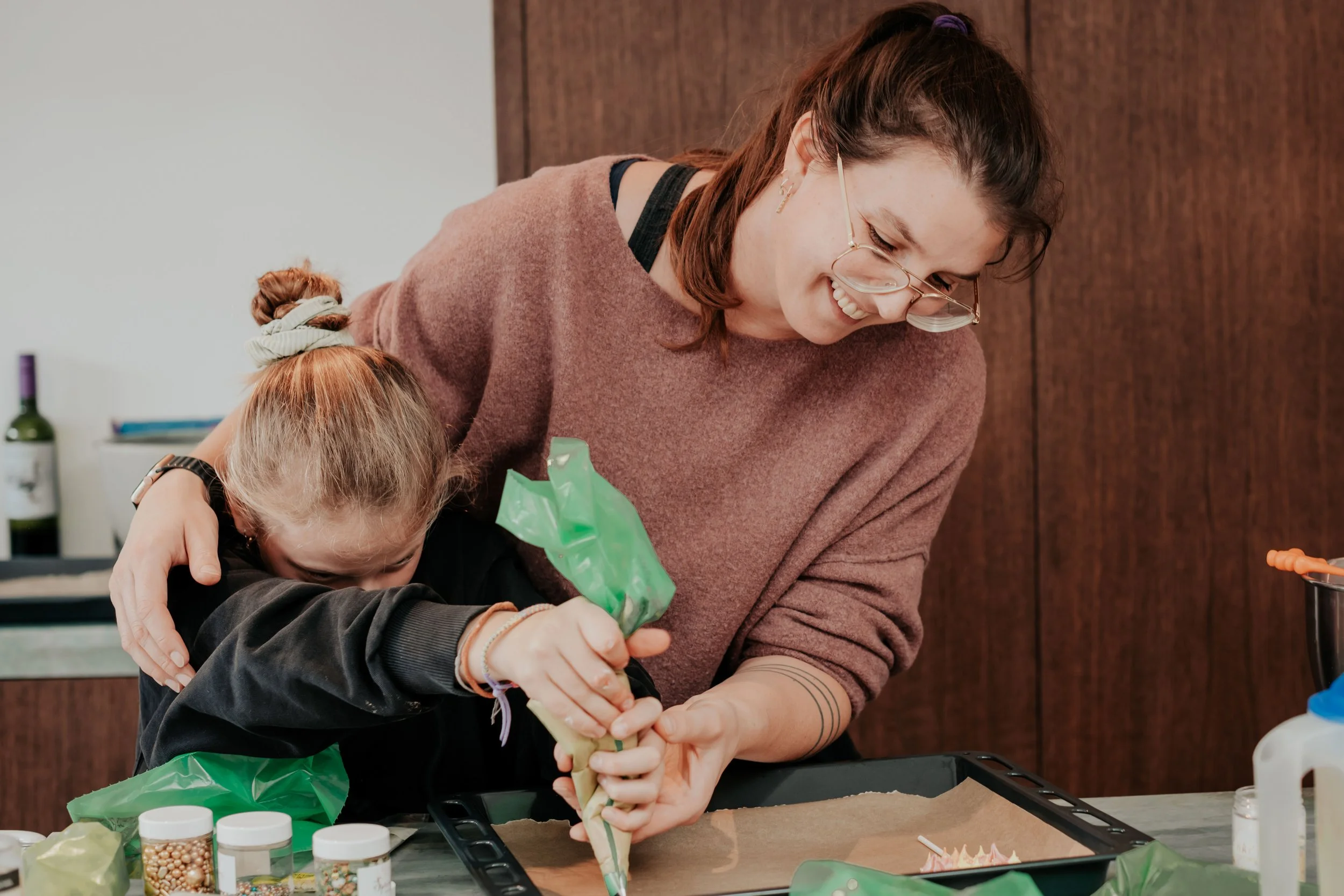 A woman and a young girl decorating a cake together in a kitchen.